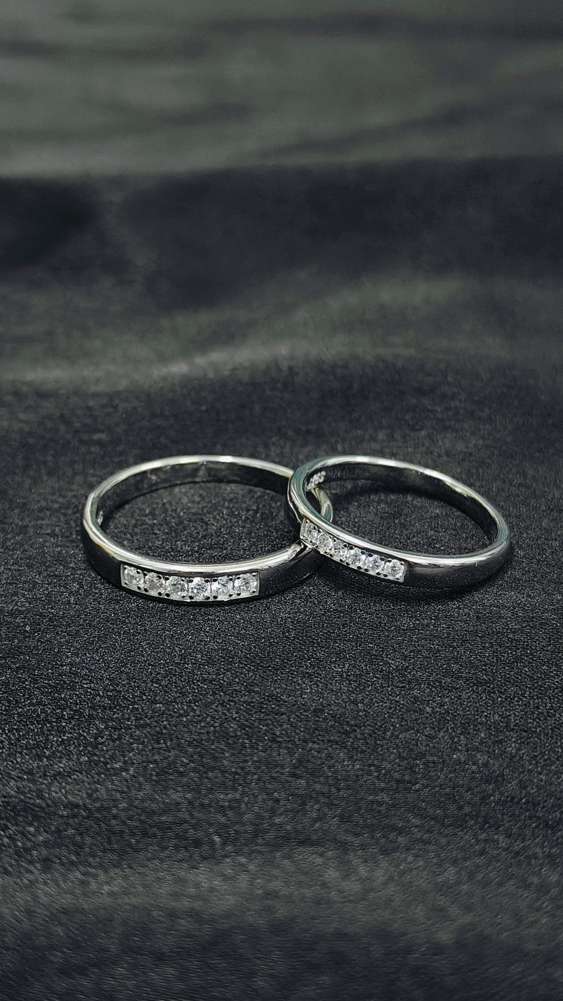 Two silver rings with small diamonds on a dark fabric background